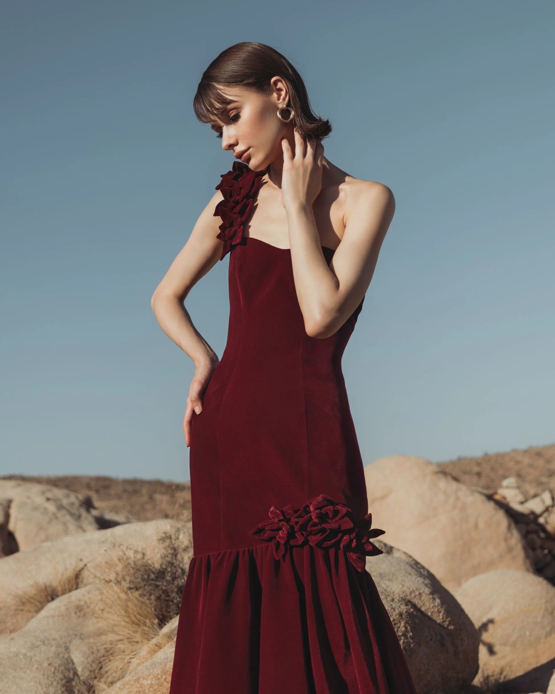 Close-up of burgundy velvet one-shoulder mermaid gown with floral appliqué detailing at shoulder and hip