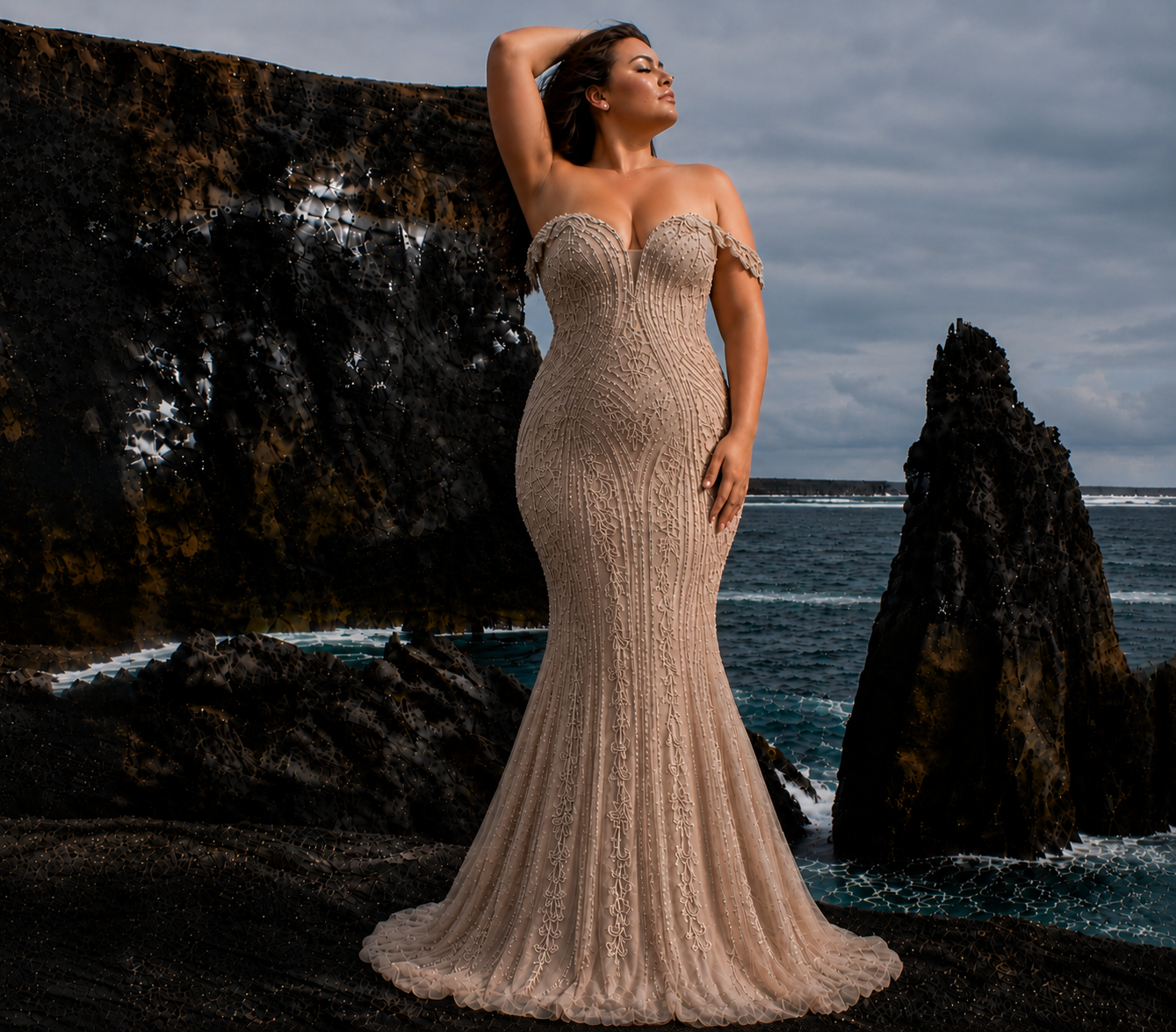 Plus size model standing on rocky beach wearing a champagne beaded mermaid gown